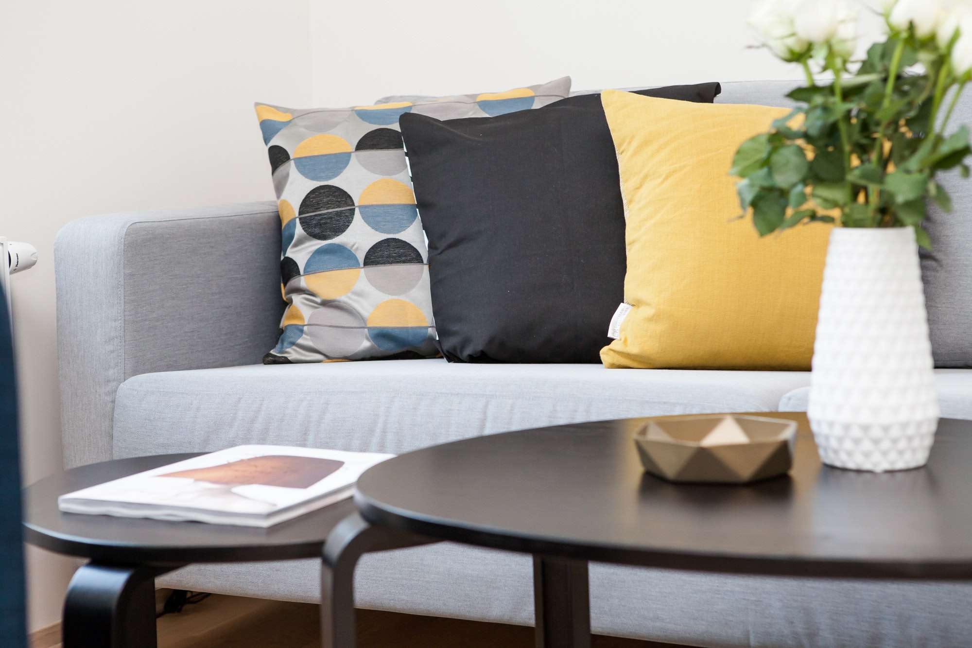 Close up shot of a living room table with a flower vase on top. There is a couch in the background with 3 cushions.