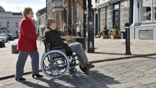 Elderly man in a wheelchair being assisted by a woman