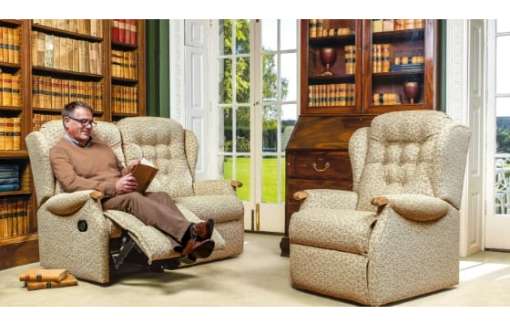 Elderly man indoors in a living room sat on a rise and recliner chair with an empty riser recliner opposite him. The room is carpeted.