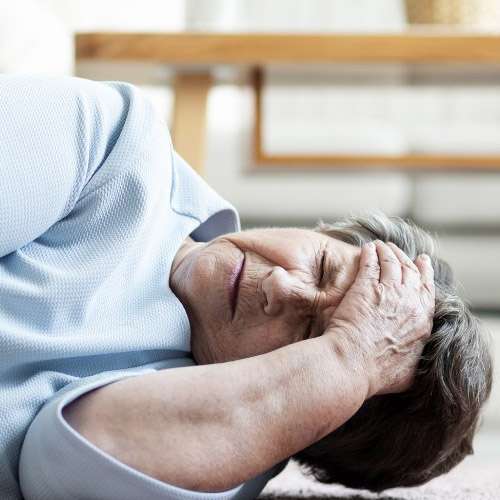 Elderly woman who has fallen to the floor. She is holding her forehead.