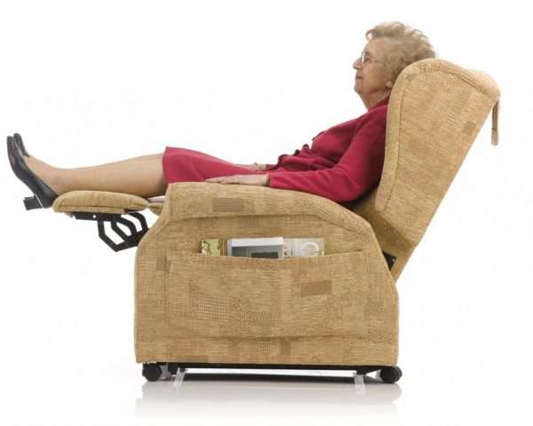 Elderly woman sitting in a riser recliner armchair. The background is white.