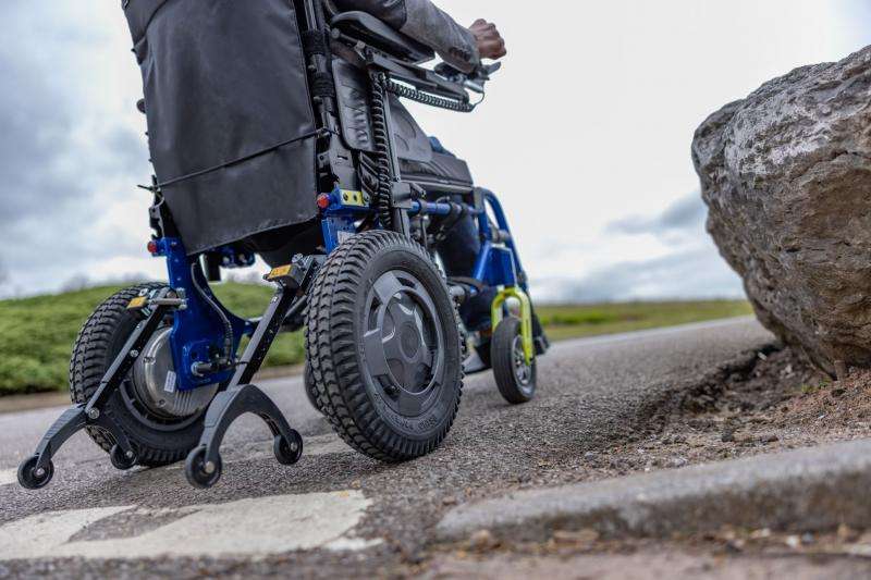 Close up of the rear wheelch on the Esprit power wheelchair. The wheelchair is in transit with a man sitting on it. The picture is taken outdoors.