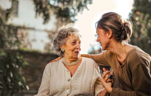 Elderly woman talking a a younger woman. They are both sat down.