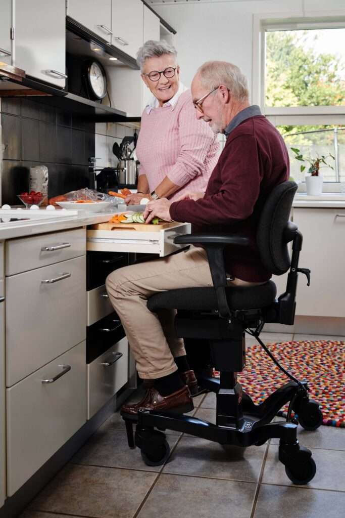Lifestyle shot of an elderly man and woman in their kitchen cooking. The man is sat on the Vela Tango 700 activity chair.