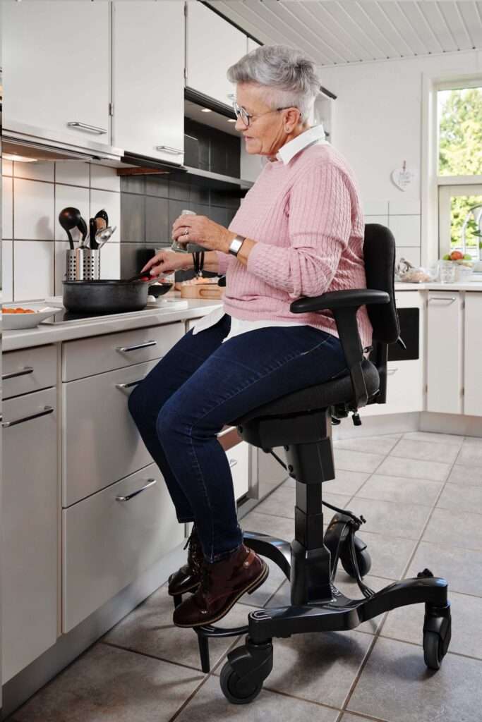 Lifestyle shot of an elderly woman on the Vela Tango 700 activity chair in her kitchen.