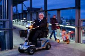 A man driving a mobility scooter at night time - the headlamp and rear lights are illuminated