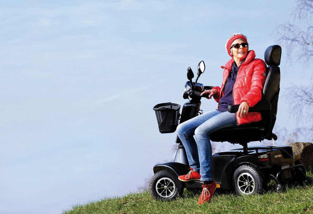 A lady sat on a mobility scooter at the edge of a lake