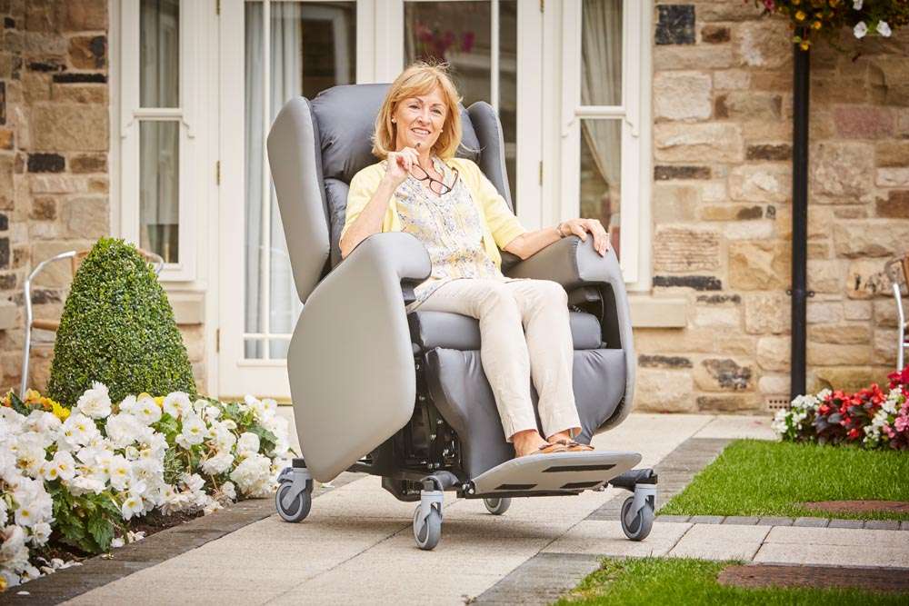 A lady sat in a care chair out in the garden.