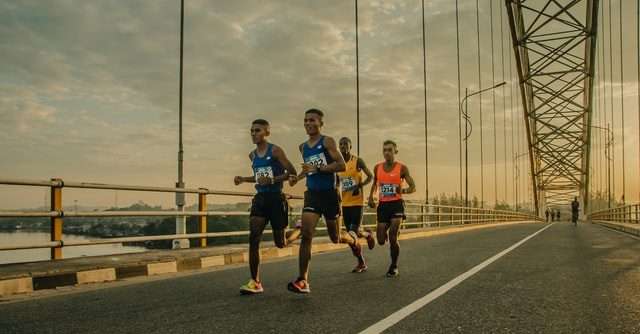 Four men running over a bridge.