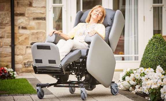 Elderly woman leaning back and using the tilt in space feature on the mobile Lento care chair with wheels, she is sat outside