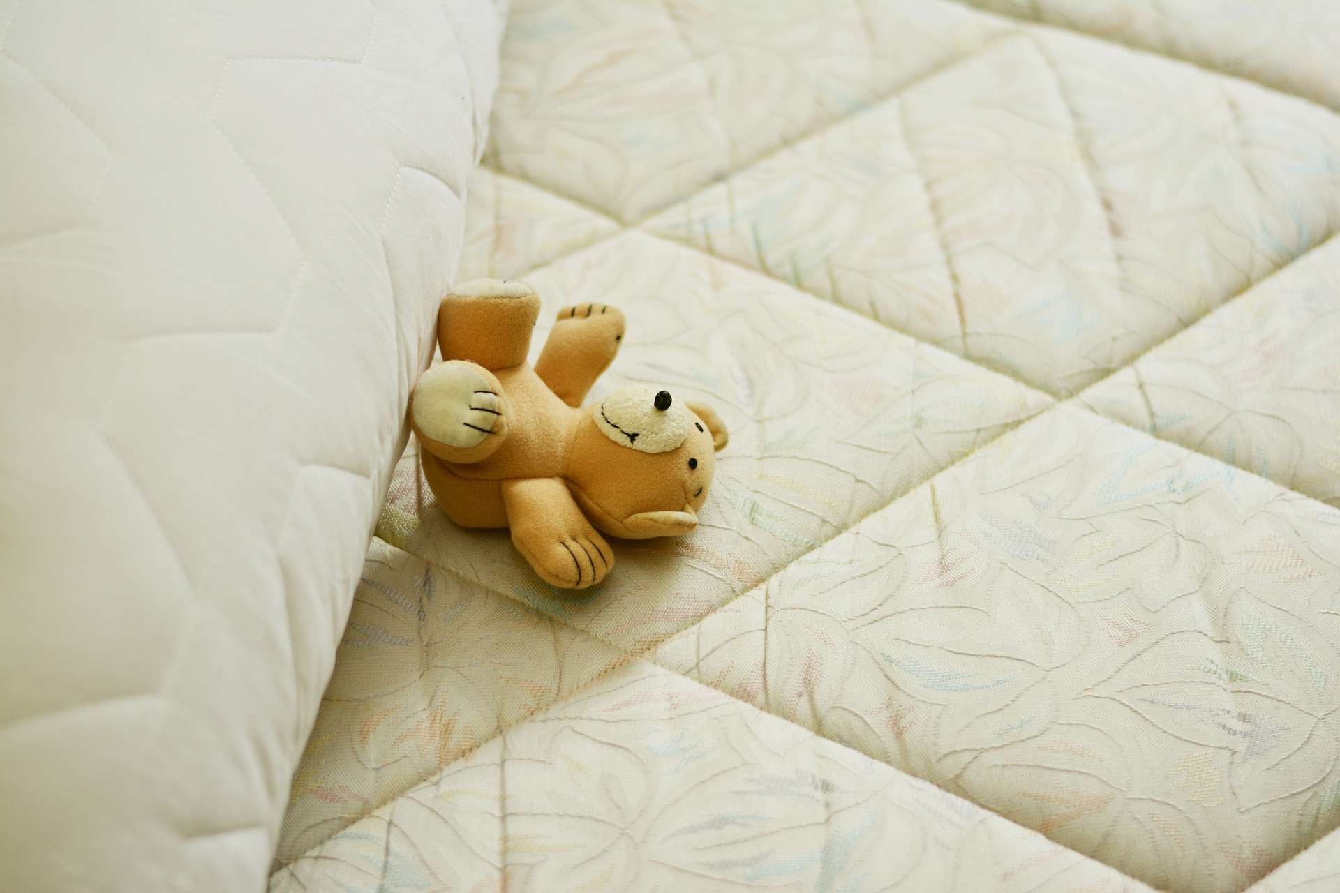 A teddy bear laid flat on a mattress