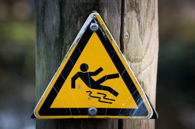 A yellow triangular warning sign showing a person slipping and falling over.