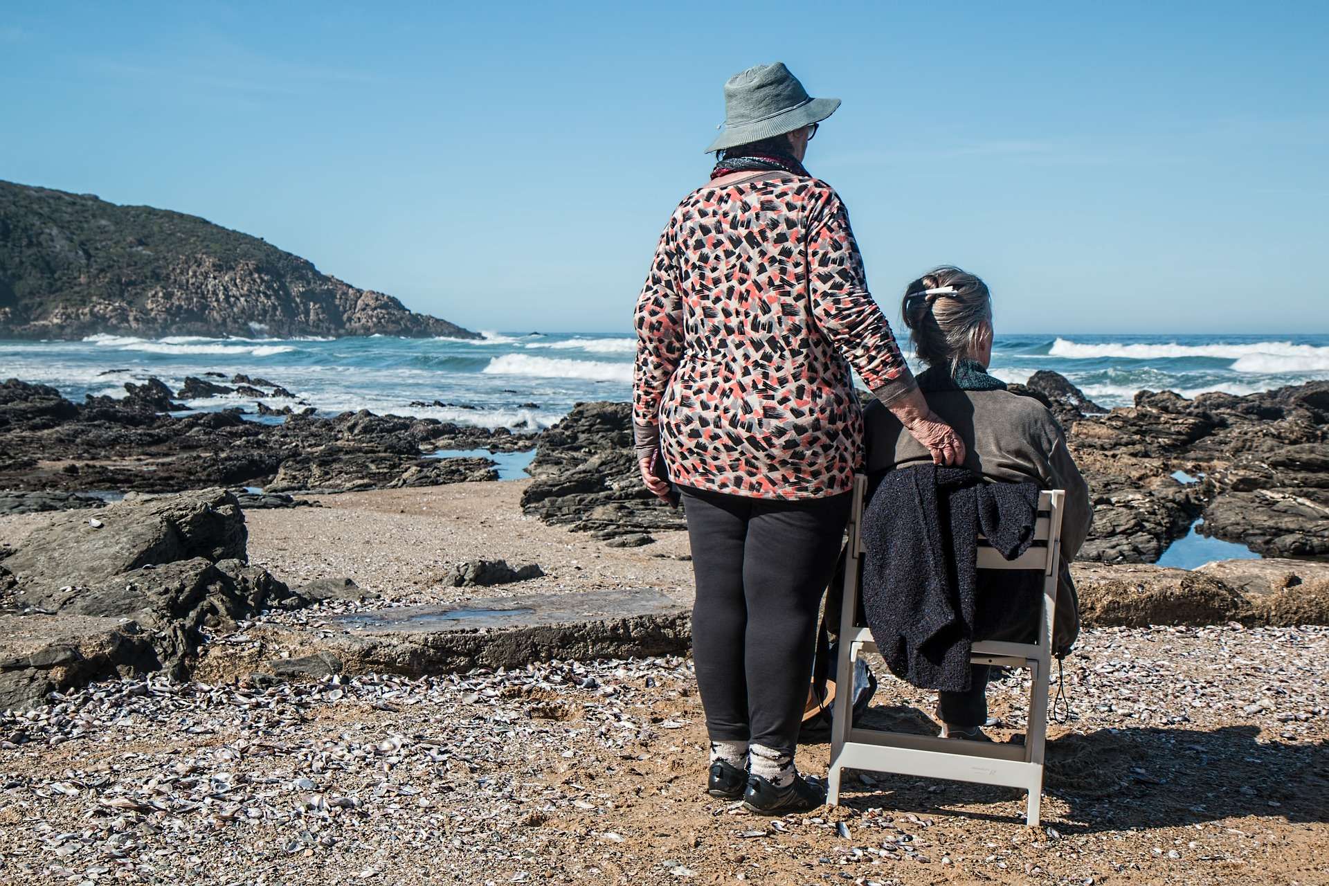 Two ladies sat together on a chair by the sea.