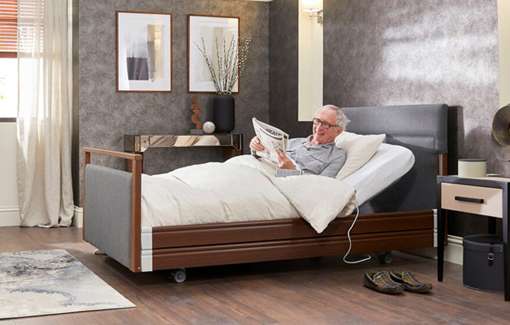 Elderly man reading in an electric profiling care bed.