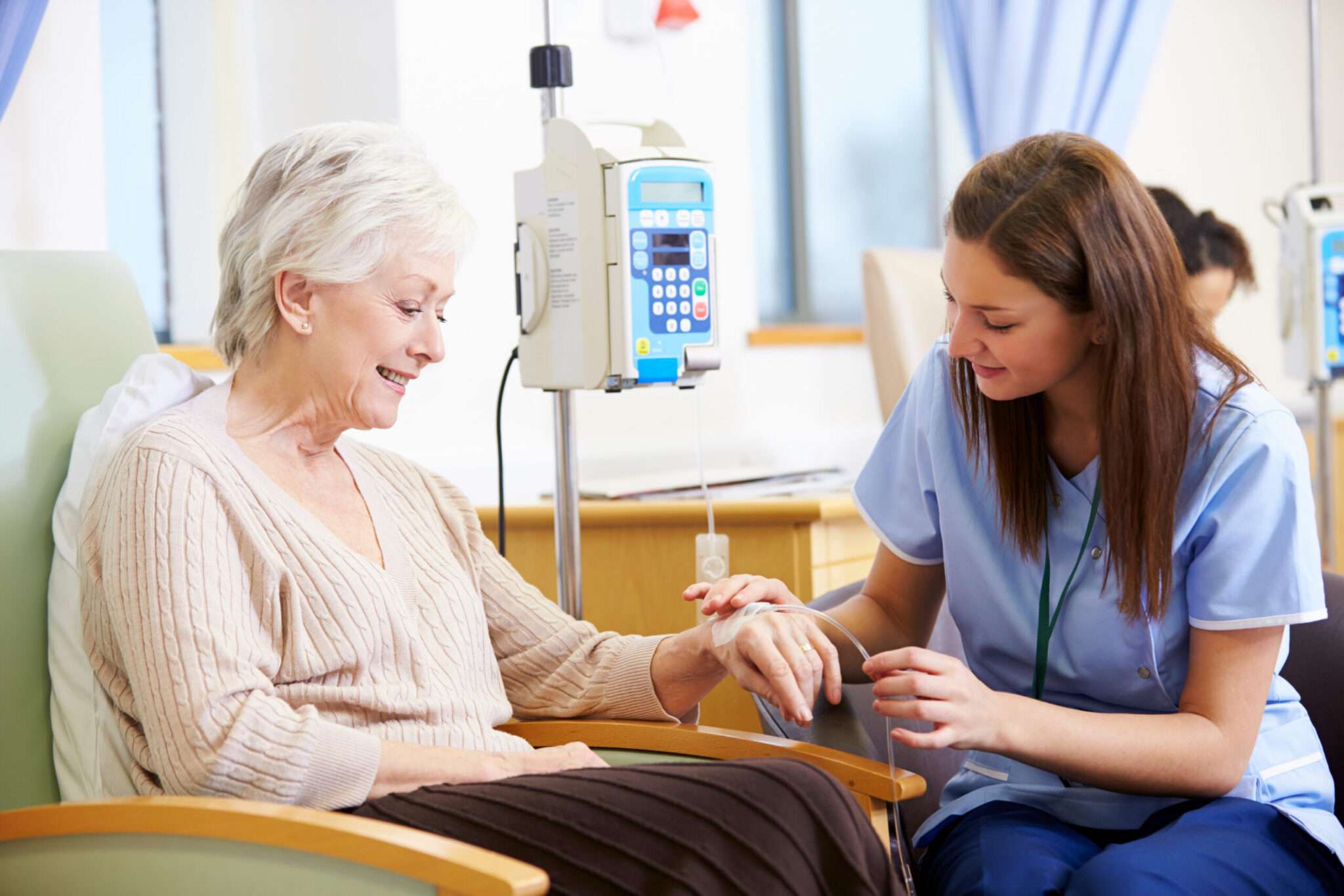 Elderly woman receiving infusion therapy treatment in a chair from a nurse.