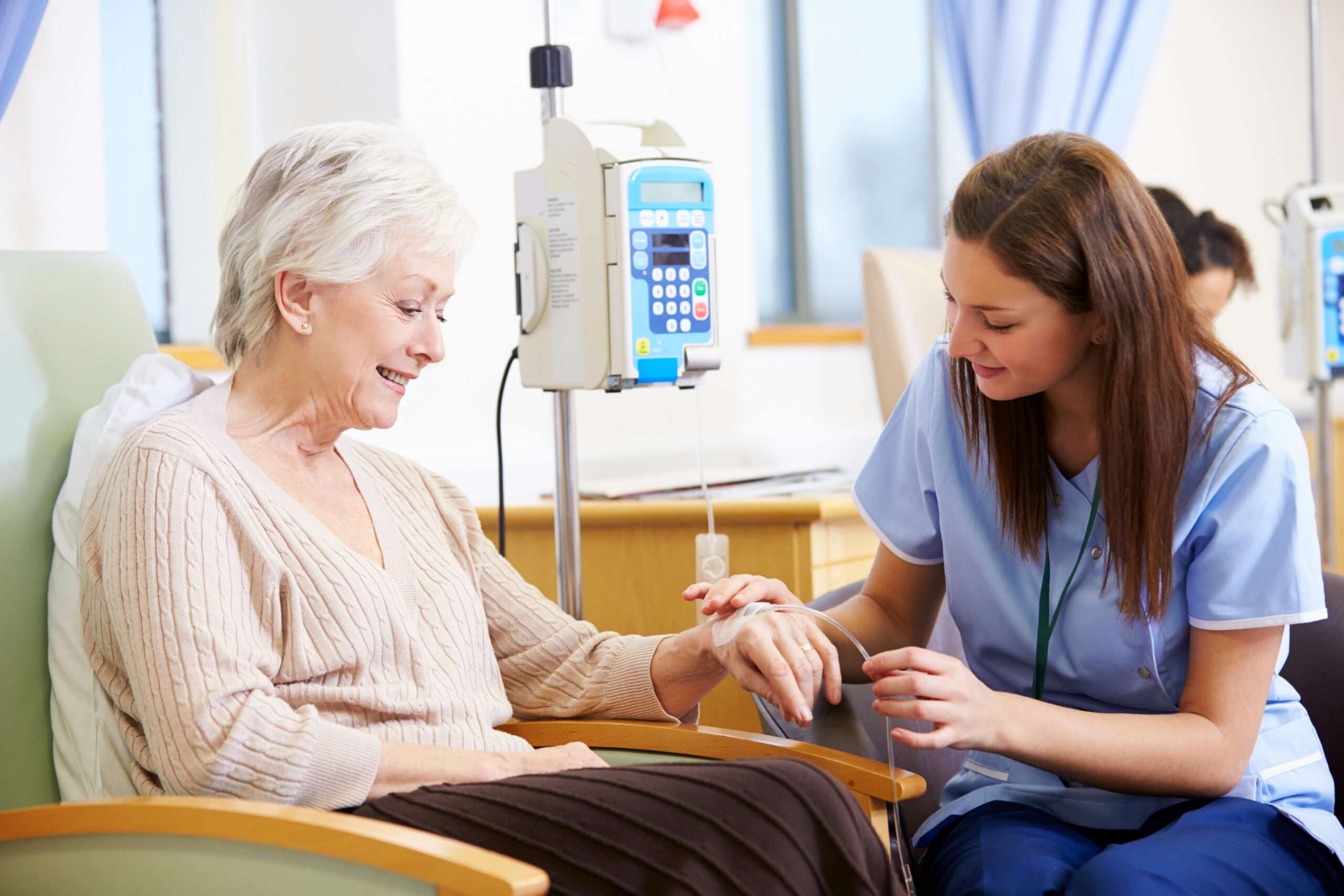 Elderly woman receiving infusion therapy treatment in a chair from a nurse. 