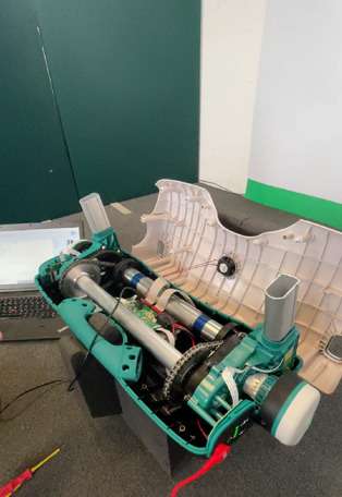 The electrical mechanisms of a Raizer patient lifting chair being repaired in a workshop with tools in the background.