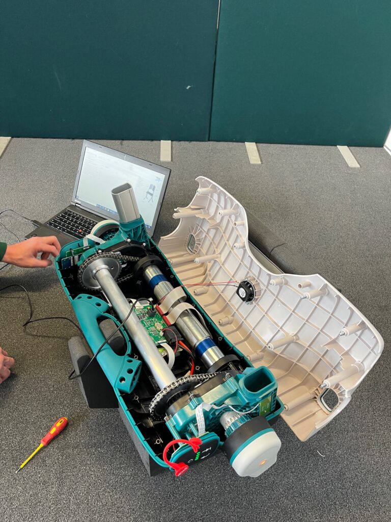 The electrical mechanisms of a Raizer patient lifting chair being repaired in a workshop with tools in the background.