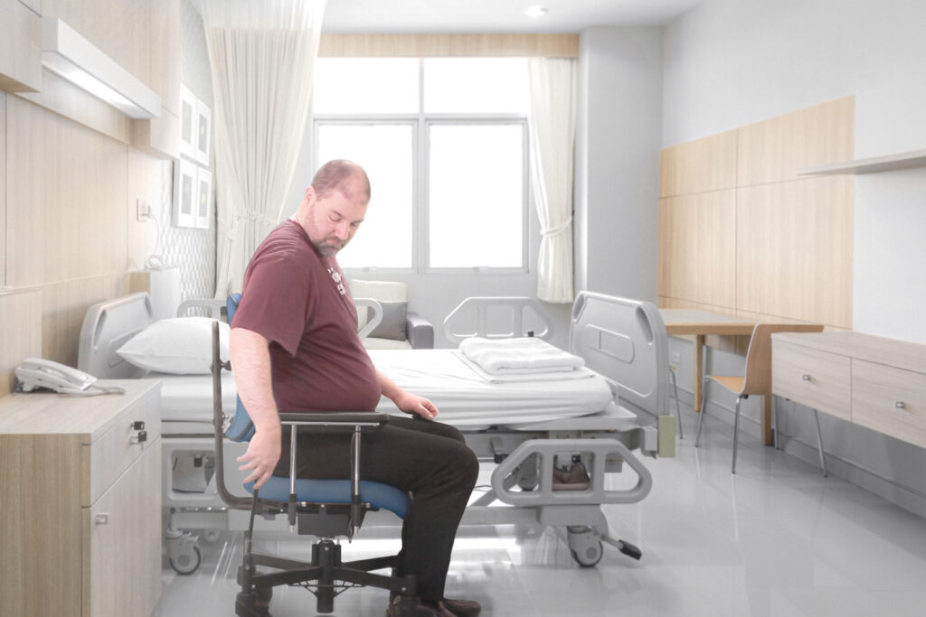 Man in a hospital using the handbrake on the VELA bariatric+ electric lift up patient chair with braked wheels.