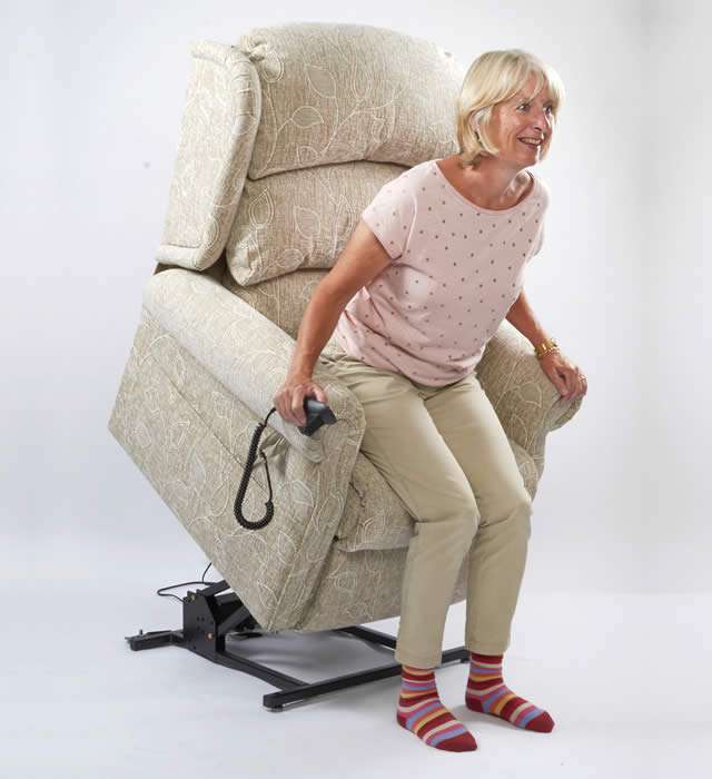 Older person (woman) using an electric riser recliner chair to help her stand up.