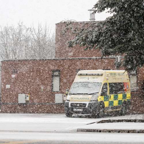 English ambulance parked outside a hospital while it is smowing.