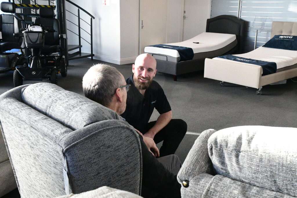 Man sat in a riser recliner chair, speaking to a salesman in the Vivid Care Harrogate mobility shop showroom.