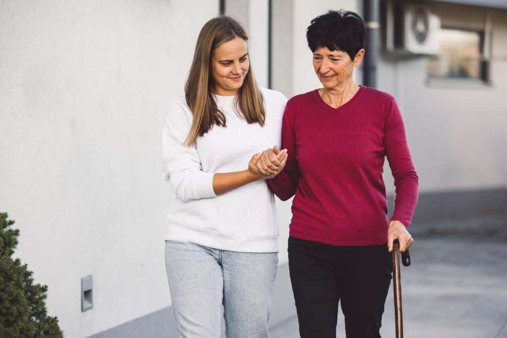 Young woman working as a home nurse taking care of a senior lady who is having trouble walking