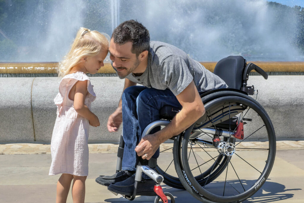 Man in a Quickie QS7 R wheelchair leaning down to talk to his young daughter