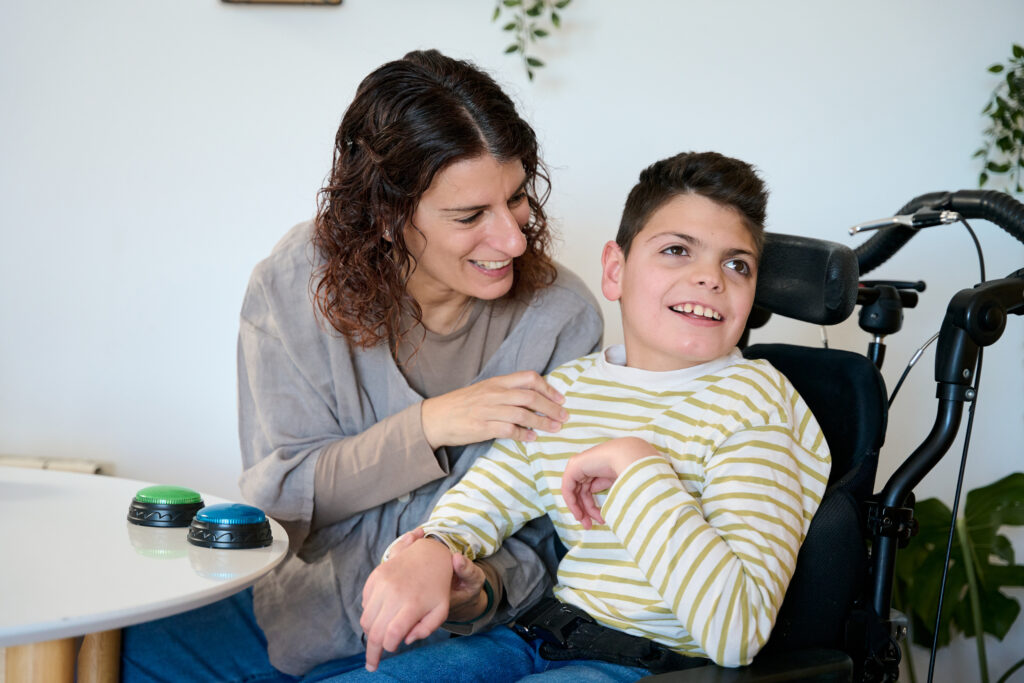 Mother supporting son with cerebral palsy using communication buttons
